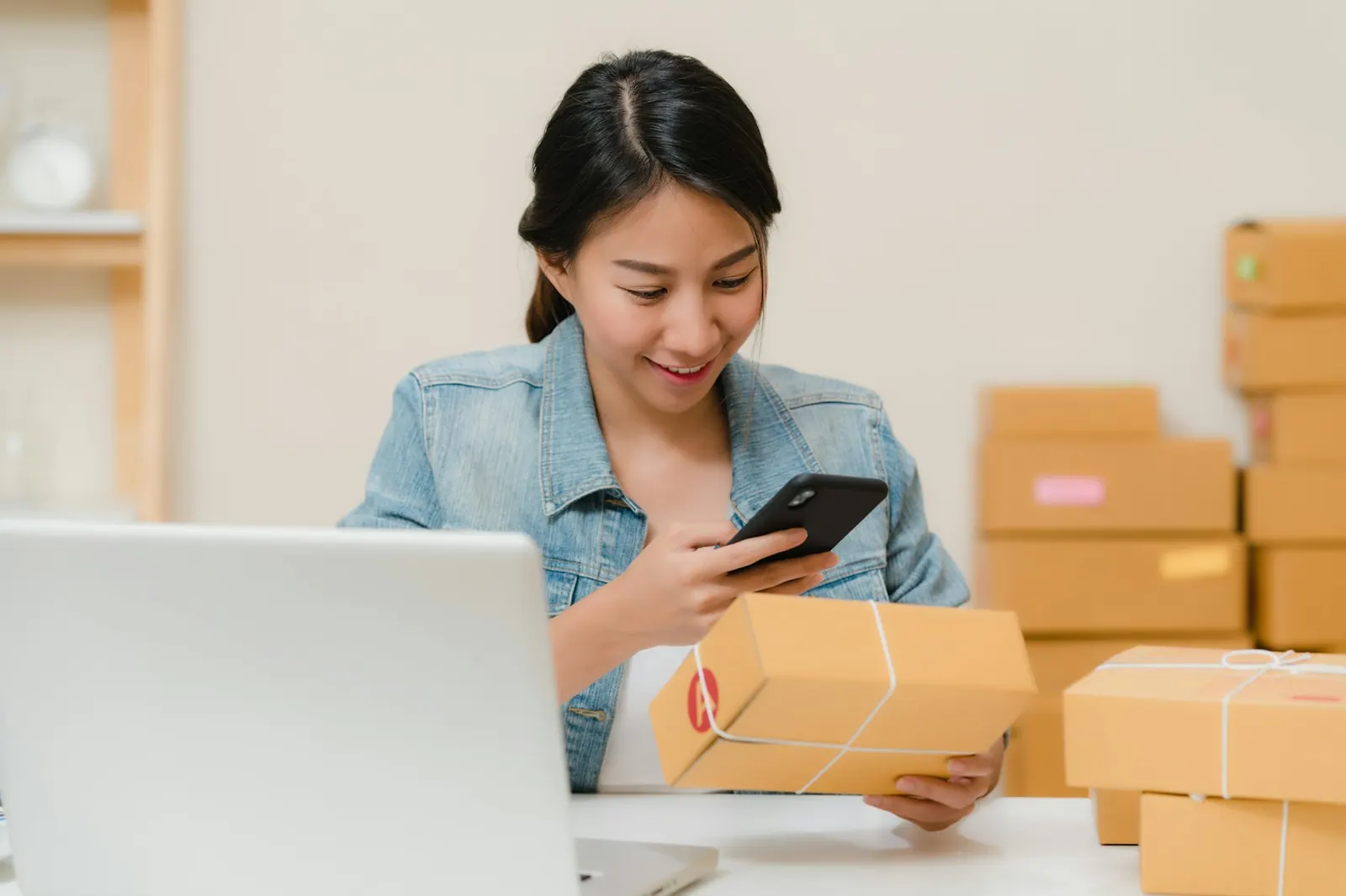 Emprendedora revisando un pedido en su teléfono junto a cajas listas para enviar